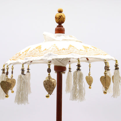 Zijaanzicht van witte canvas Bali-parasol met gouden versieringen en houten handvat, 68 cm hoog, bohemien tropisch woonaccessoire
