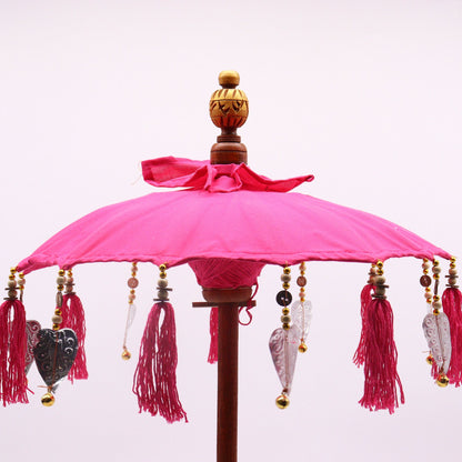 Bovenaanzicht van een Balinese parasol met levendig roze katoen en kwastjes, een traditionele Indonesische decoratieve paraplu.
