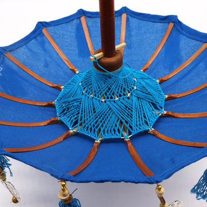 Bovenaanzicht van een Balinese parasol met levendig turquoise katoen en kwastjes, een traditionele Indonesische decoratieve paraplu.
