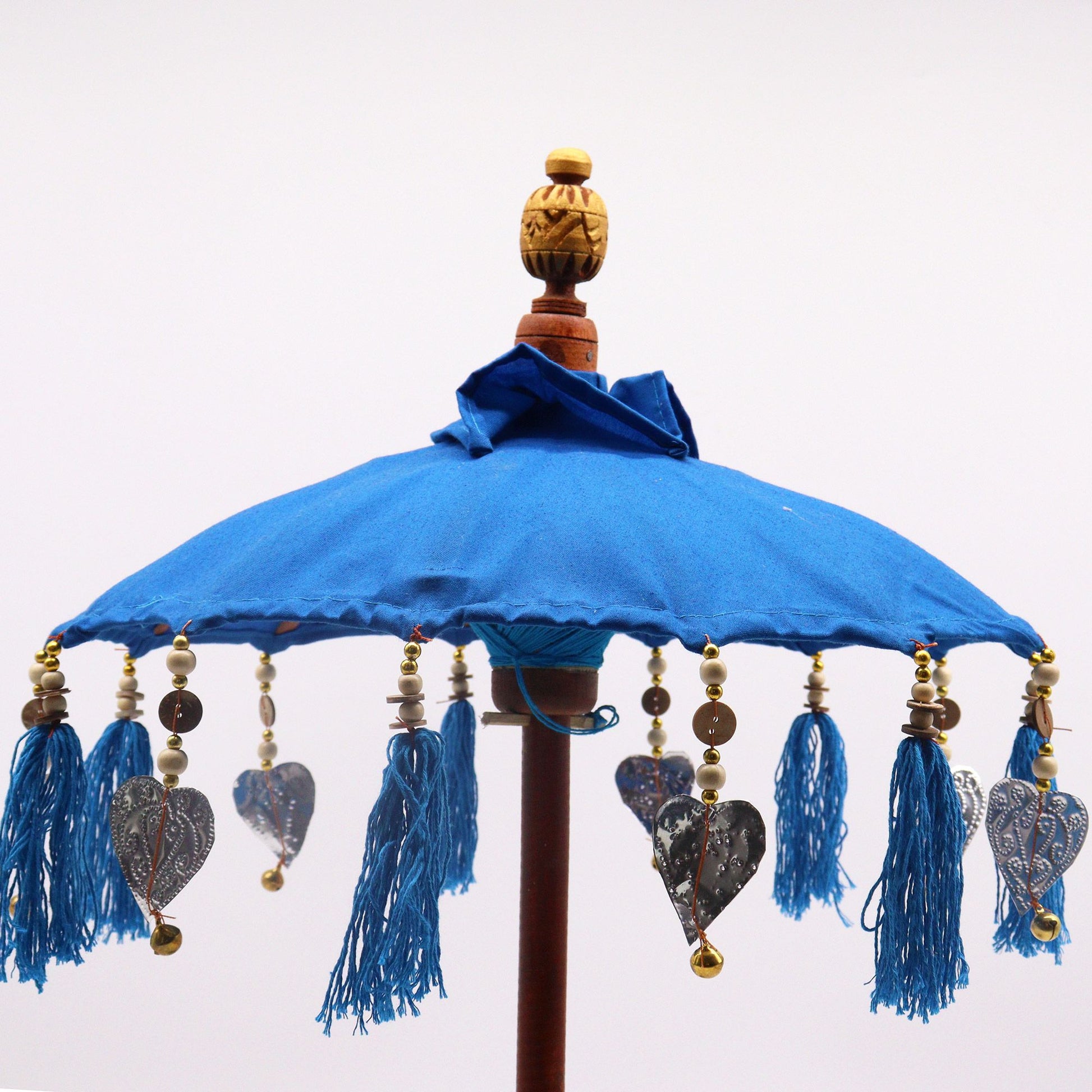 Detailfoto van kleurrijke kwastjes en turquoise katoenen textuur op een Balinese parasol, handgemaakt bohemien woonaccessoire voor aan zee.
