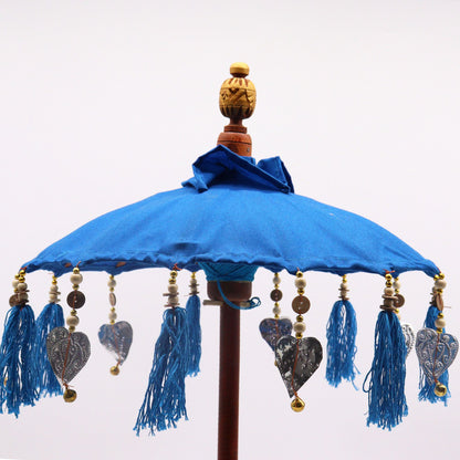 Detailfoto van kleurrijke kwastjes en turquoise katoenen textuur op een Balinese parasol, handgemaakt bohemien woonaccessoire voor aan zee.
