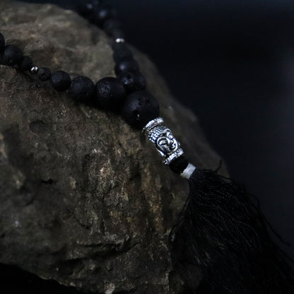 Close-up van een ketting van vulkanisch lavasteen met een delicate zilveren Boeddha-bedel die innerlijke rust en wijsheid symboliseert.
