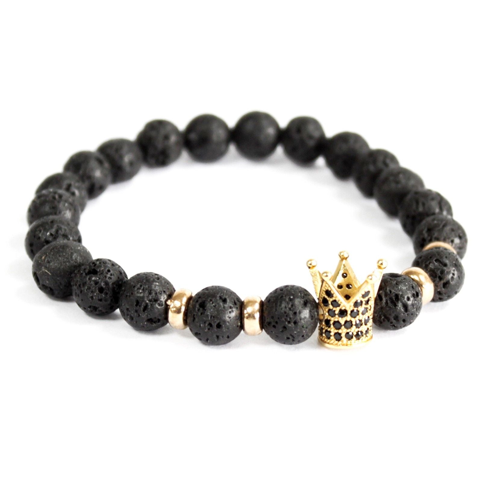 Lava stone gouden kroon armband met natuurlijke zwarte vulkanische kralen en gouden kroon bedeltje op witte achtergrond, elastische bohemian sieraden voor gronding en transformatie van het wortelchakra.

