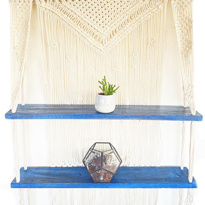 Bohemian macramé hangende plank met blauwe accenten waarop woonaccessoires worden tentoongesteld
