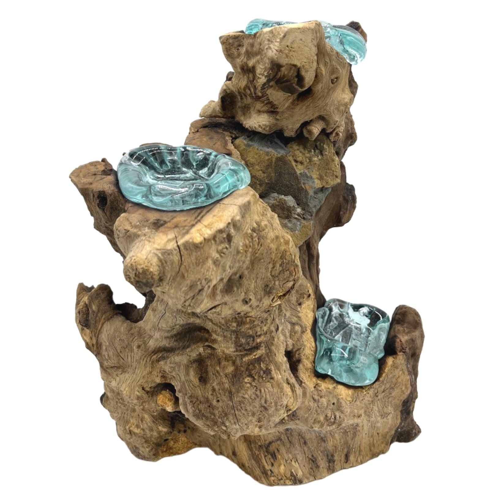 Close-up van een drievoudige kandelaar van gesmolten glas, met handgeblazen houders van gerecycled glas die zijn versmolten met een natuurlijke houtwortel, traditioneel Balinees sculpturaal vakmanschap.
