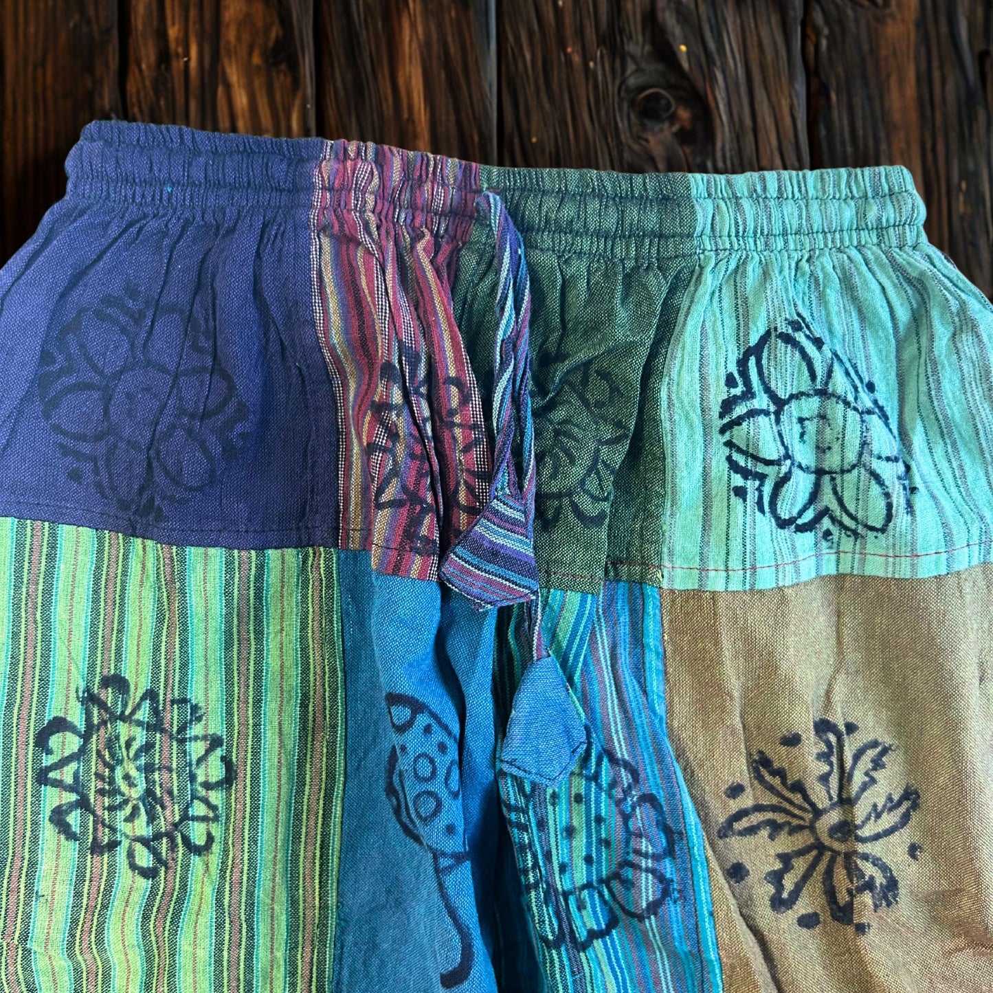 Detail van hemelsblauwe en blauwgroene patchworkdelen met paddenstoelenmotieven op een broek in aardetinten
