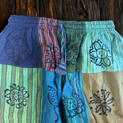 Detail van hemelsblauwe en blauwgroene patchworkdelen met paddenstoelenmotieven op een broek in aardetinten
