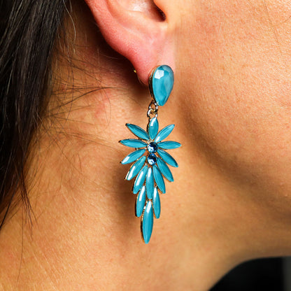 Close-up van een langere oorbel van blauwgroen glas met een gelaagd ontwerp dat subtiel schittert en natuurlijke elegantie uitstraalt.
