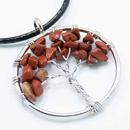 Close-up van rode jaspis Tree of Life-hanger met aardse rode edelsteenachtergrond en metalen boomsymbool voor healing van het wortelchakra
