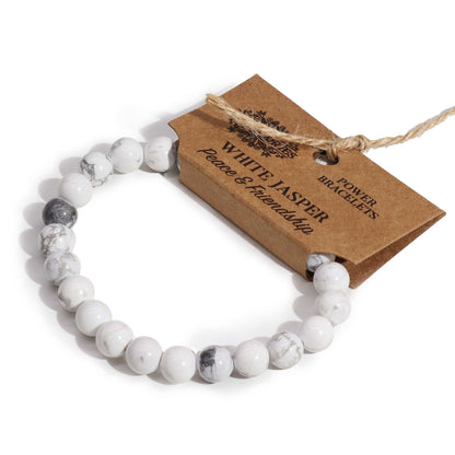 Witte jaspis power armband met natuurlijke puur witte edelstenen op een witte achtergrond met houten cadeaulabel, elastische healing sieraden voor helderheid en rust in het kruinchakra.
