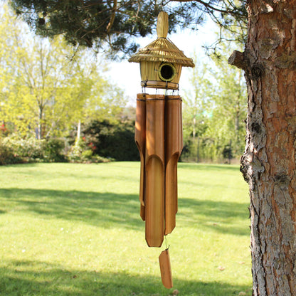 Full view of large seagrass bird box in garden setting with natural bamboo chimes
