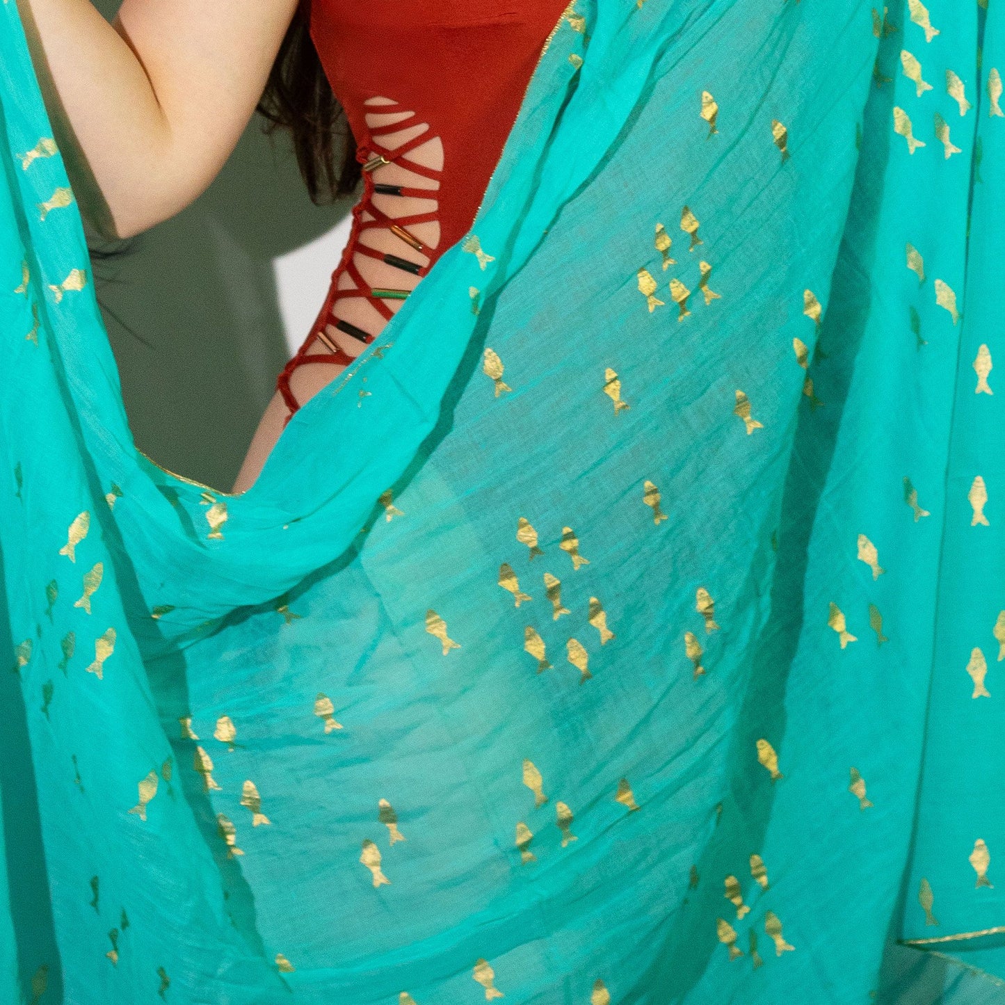 Close-up detail van handbeschilderd gouden vispatroon op turquoise sari katoen pario
